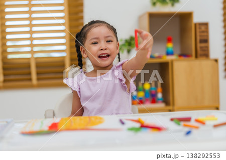 happy preschool child girl drawing and painting with colorful oil pastels on paper 138292553