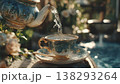 Close-up of hot water being poured from a decorative teapot into a vintage teacup and saucer, set in a sunny garden. 138293264