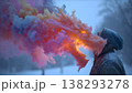 A person exhales colorful smoke that forms a dragon shape in a snowy winter landscape. 138293278