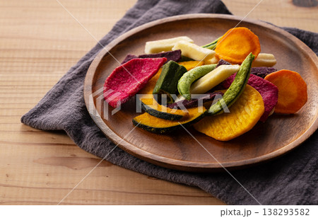 木製プレートと布のある食卓に盛られた色鮮やかな野菜チップス ライフスタイル 138293582