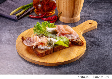 Gourmet rye bread toast with cured meat, soft cheese, and capers on a wooden board. Gourmet rye bread toast with cured meat, soft cheese, and capers on a wooden board. 138294089