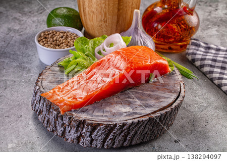 Fresh raw salmon fillet on a rustic wooden slice with lime, garlic, coriander, and onion for cooking. 138294097