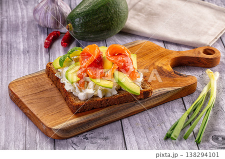 Smoked salmon and avocado toast with cream cheese on a rustic wooden cutting board. 138294101