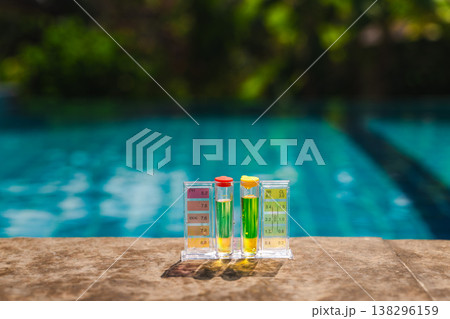 Pool water testing kit measuring pH and chlorine levels placed on pool edge with blue swimming pool background Pool water testing kit measuring pH and chlorine levels placed on pool edge with blue swimming pool background 138296159
