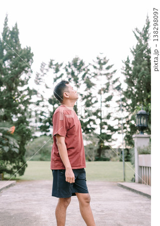 Southeast Asian man looking sideways and up in relaxed outdoor setting 138298097