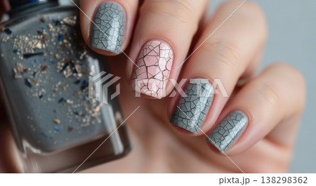 Close-up of a hand holding a bottle of glitter polish, featuring a grey and pink crackle-effect manicure with fine line details. Close-up of a hand holding a bottle of glitter polish, featuring a grey and pink crackle-effect manicure with fine line details. 138298362