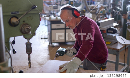Senior carpenter drilling wood plank in workshop 138298455
