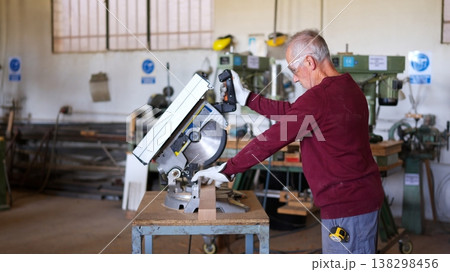 Senior carpenter cutting wood using miter saw in workshop 138298456