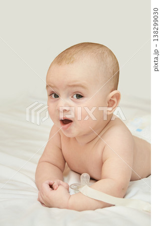 Caucasian Baby Lying On Stomach On White Bed, Wearing Diaper, Expressing Surprise, Indoor Soft 138299030