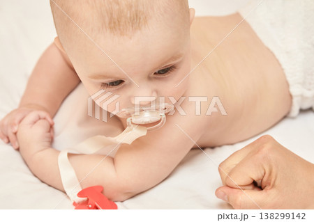 Caucasian Male Baby With Pacifier Lying On Stomach In White Diaper On Bed, Arm Fist Close-Up 138299142