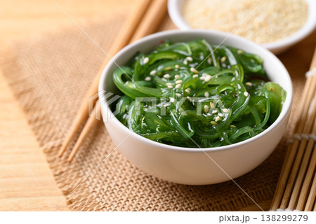 Fresh Japanese seaweed salad (Chuka Wakame) in a white bowl and chopsticks on wooden background 138299279
