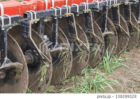 Close up of agricultural disc harrow blades cutting soil with grass in field during cultivation 138299328