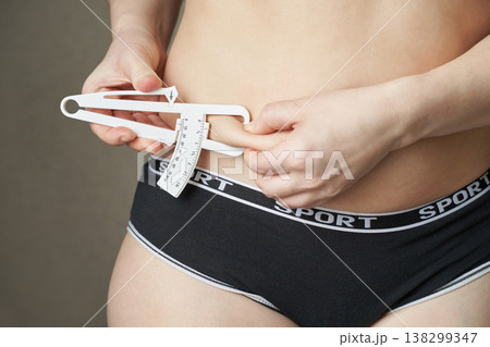 Young caucasian female measuring body fat with caliper in fitness apparel for health monitoring Young caucasian female measuring body fat with caliper in fitness apparel for health monitoring 138299347