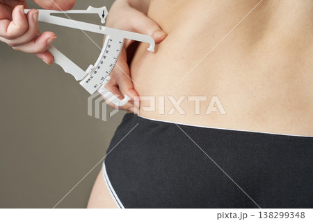 Female using caliper to measure body fat on waist for fitness monitoring and weight management Female using caliper to measure body fat on waist for fitness monitoring and weight management 138299348