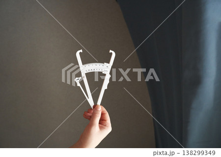 Hand holding calipers indoors against grey and blue background, highlighting precision 138299349