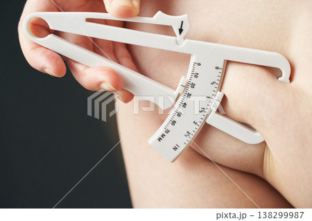 Female hand measuring body fat with caliper on skin close-up analysis tool Female hand measuring body fat with caliper on skin close-up analysis tool 138299987