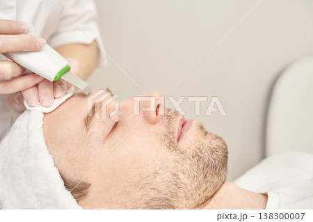 Male caucasian adult receiving facial treatment with ultrasonic skin scrubber in spa setting Male caucasian adult receiving facial treatment with ultrasonic skin scrubber in spa setting 138300007
