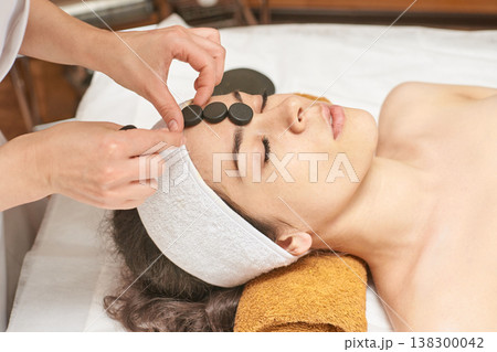 Young Caucasian Female Relaxing With Hot Stone Therapy At Spa For Facial Rejuvenation And Skin Care 138300042