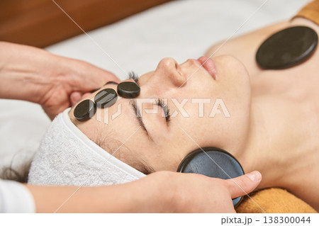 Young Caucasian Female Enjoying Hot Stone Facial Massage At Spa For Relaxation And Wellness 138300044