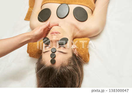 Young Caucasian Female Relaxing With Hot Stone Therapy In Spa For Relaxation And Wellness Young Caucasian Female Relaxing With Hot Stone Therapy In Spa For Relaxation And Wellness 138300047