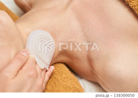 Female Applying Exfoliating Brush To Neck And Shoulder For Skin Care And Relaxation 138300050