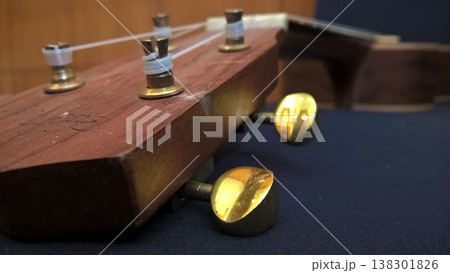 Acoustic instrument wooden headstock metal tuning peg string closeup music detail warm tone macro focus craftsmanship traditional design studio backdrop 138301826