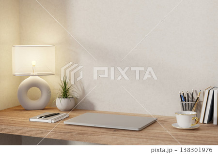 Closed laptop with book and pencil aside hollow lamp and potted plant on wooden table at room corner 138301976