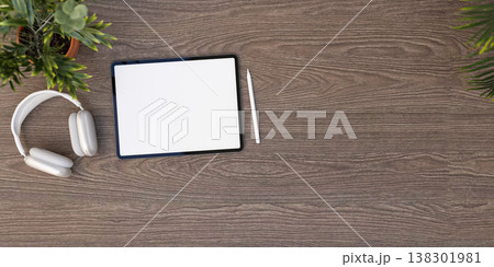 Top view of white screen tablet with stylus pencil and headphones aside potted plant on wooden table Top view of white screen tablet with stylus pencil and headphones aside potted plant on wooden table 138301981
