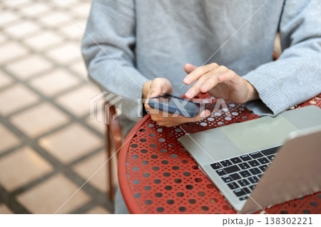 Close up of a hand holding phone scrolling through social media watching video over laptop on table. Close up of a hand holding phone scrolling through social media watching video over laptop on table. 138302221
