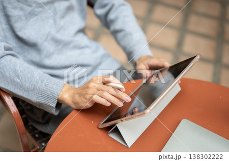 Close up of man's hand holding pen touching a tablet on round brown table while sitting in the cafe. 138302222