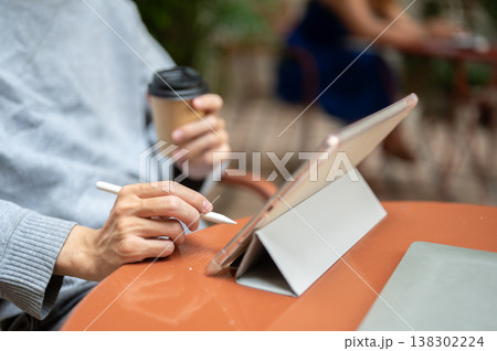 Close up of man's hand holding coffee writing drawing on tablet on table while sitting in the cafe. 138302224