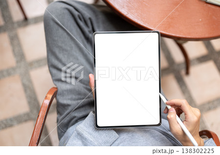 Top view of hand holding white screen tablet with stylus pen sitting on chair at table on tile floor 138302225