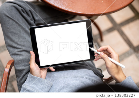 Top view of hand holding blank screen tablet and stylus pen sitting on chair at table on tiles floor 138302227