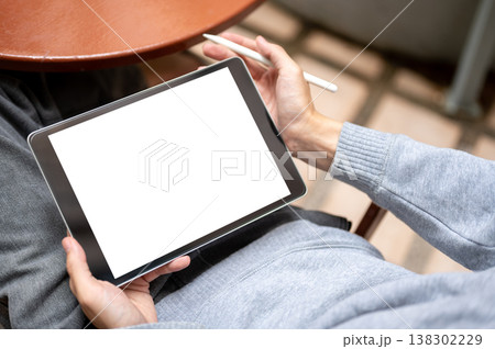Top view of hands holding blank screen tablet and stylus pen sitting on chair at table on tile floor 138302229