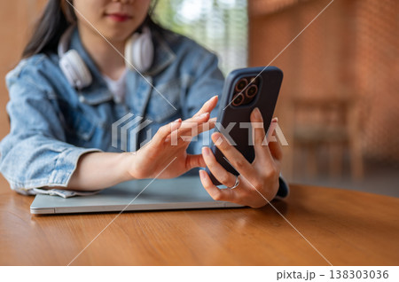 Close up of blurred asian woman holding and touching on phone while sitting at wooden table in cafe. Close up of blurred asian woman holding and touching on phone while sitting at wooden table in cafe. 138303036