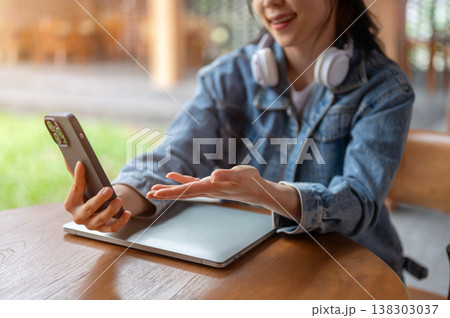 Close up of blurred woman holding phone talking on video call while sitting at wooden table in cafe. Close up of blurred woman holding phone talking on video call while sitting at wooden table in cafe. 138303037