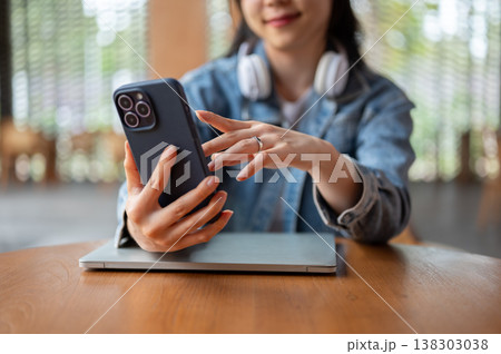Close up of blurred woman looking at phone holding over laptop while sitting at wooden table in cafe Close up of blurred woman looking at phone holding over laptop while sitting at wooden table in cafe 138303038