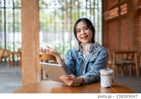 Pretty asian woman holding tablet and open palm aside coffee on wooden table while sitting in cafe. Pretty asian woman holding tablet and open palm aside coffee on wooden table while sitting in cafe. 138303047