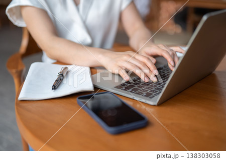 Close up of woman hands typing on laptop aside book and phone while sitting at wooden table in cafe. Close up of woman hands typing on laptop aside book and phone while sitting at wooden table in cafe. 138303058