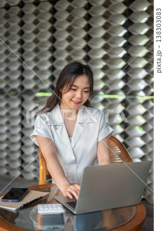 Pretty asian woman typing on laptop aside book and calculator while sitting at glass table in cafe. 138303083