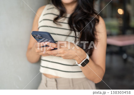 Close up of woman looking at phone holding with both hands standing at pillar in university building Close up of woman looking at phone holding with both hands standing at pillar in university building 138303458
