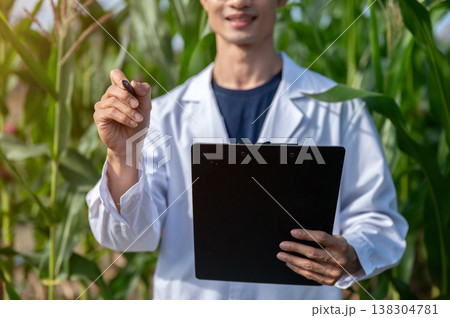 Close up of agricultural researcher man holding clipboard pointing pen while standing in crop farm. Close up of agricultural researcher man holding clipboard pointing pen while standing in crop farm. 138304781