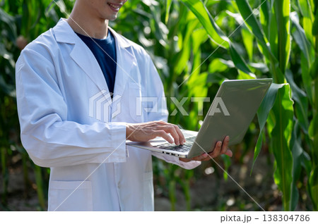Close up of agricultural researcher man holding looking at laptop while walking in green crop farm Close up of agricultural researcher man holding looking at laptop while walking in green crop farm 138304786