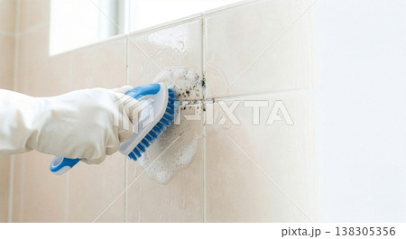 浴室のタイルの黒カビをブラシと泡で掃除するゴム手袋の手元のクローズアップ 138305356