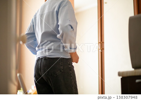 Middle aged woman in light blue shirt and dark jeans looking at her reflection in home mirror. Mature lady checking her appearance. Concept of self care and fashion styling at home. 138307948
