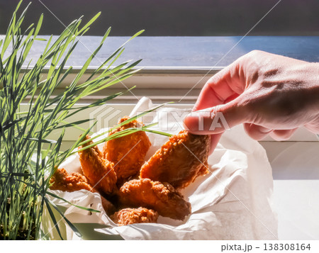 Man hand grabbing crispy fried chicken wing from bowl. Fast food snack served in paper. Homemade meal preparation, culinary concept. Greasy appetizer, protein dish, kitchen interior. Man hand grabbing crispy fried chicken wing from bowl. Fast food snack served in paper. Homemade meal preparation, culinary concept. Greasy appetizer, protein dish, kitchen interior. 138308164