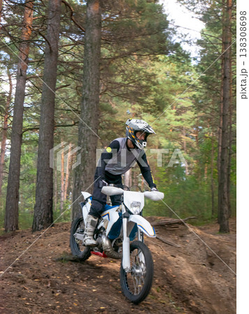 Motorcyclist riding dirt bike through pine forest. Biker in protective gear driving off-road motorcycle on trail. Extreme sport activity and active hobby in nature during summer day. Motorcyclist riding dirt bike through pine forest. Biker in protective gear driving off-road motorcycle on trail. Extreme sport activity and active hobby in nature during summer day. 138308698