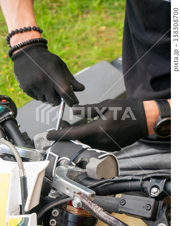 Mechanic repairing motorcycle handlebar with tool. Man fixing motorbike controls using screwdriver. Outdoor vehicle maintenance, technical service, restoration and garage hobby project work. Mechanic repairing motorcycle handlebar with tool. Man fixing motorbike controls using screwdriver. Outdoor vehicle maintenance, technical service, restoration and garage hobby project work. 138308700