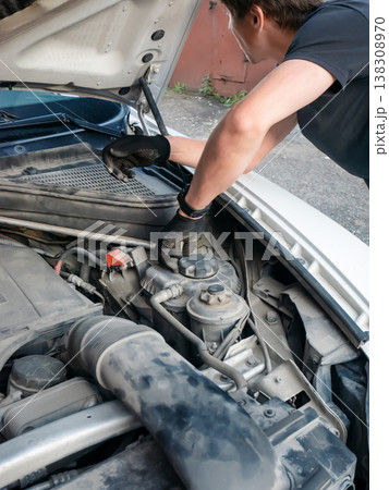 Man mechanic repairing car engine with open hood. Professional auto technician checking coolant level in vehicle. Maintenance service and automotive repair concept in workshop garage. 138308970