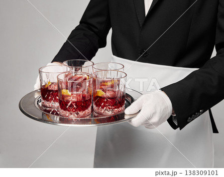 Close up of waiter hands holding tray with cocktail glasses in studio lighting. 138309101